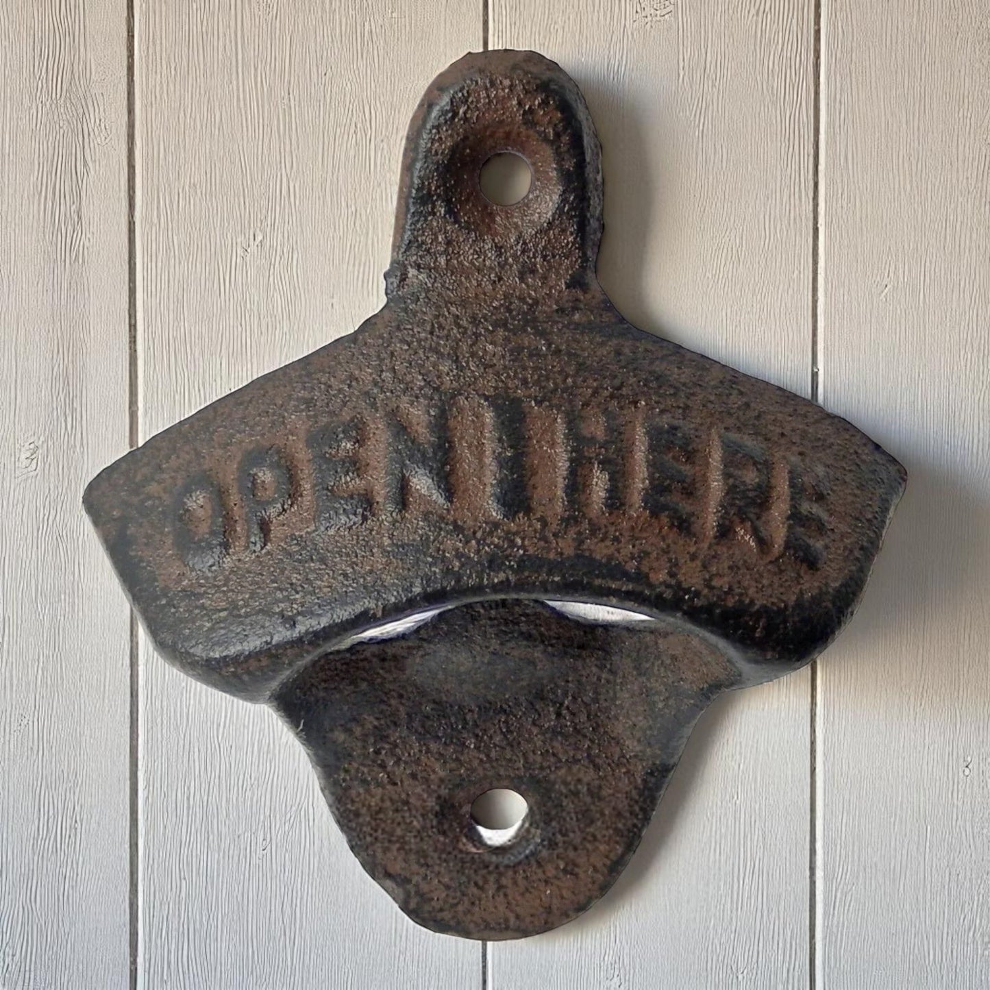 Rustic cast iron bottle opener with 'Open Here' text on a wooden background
