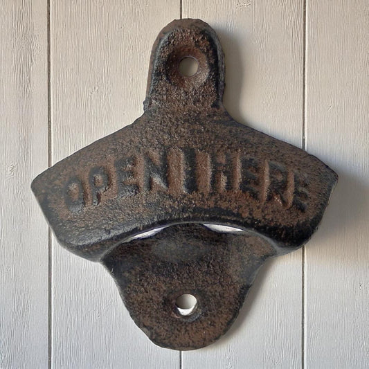 Rustic cast iron bottle opener with 'Open Here' text on a wooden background