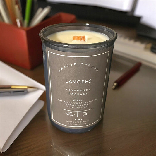 Candle labeled 'Layoffs' on a desk with office supplies in the background